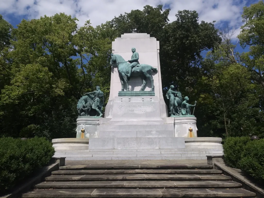 John H. Patterson Memorial at Hills & Dales MetroPark in Kettering, Ohio, surrounded by mature trees under a partly cloudy sky